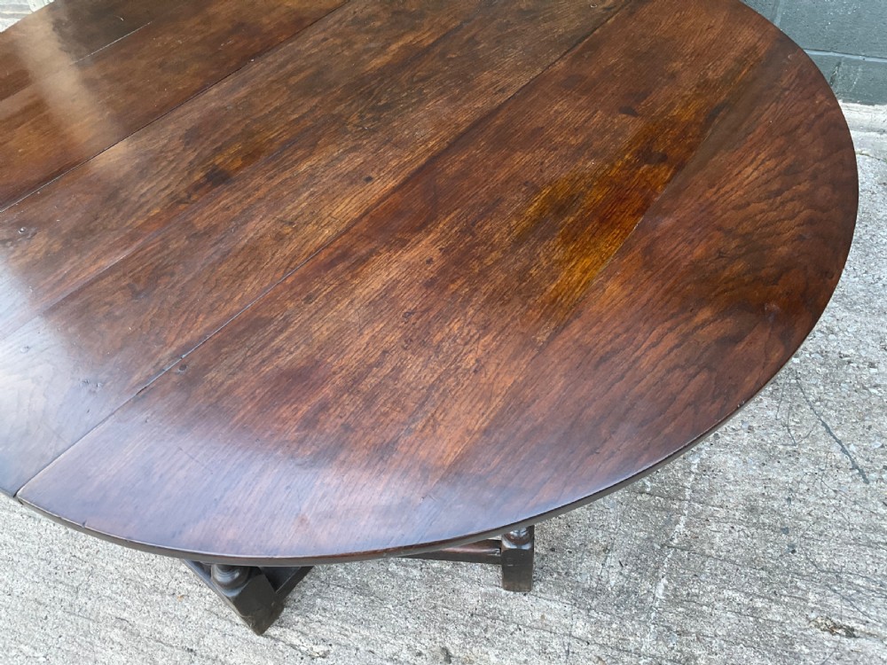 Underside view of a dark brown oak gateleg table showing baluster turned legs, stretchers, hand-forged iron hinges, and hinged drop leaves. View V