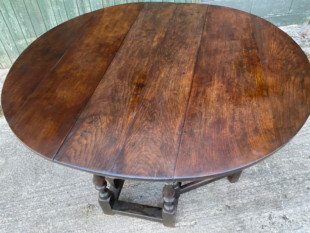 Underside view of a dark brown oak gateleg table showing baluster turned legs, stretchers, hand-forged iron hinges, and hinged drop leaves. View VI