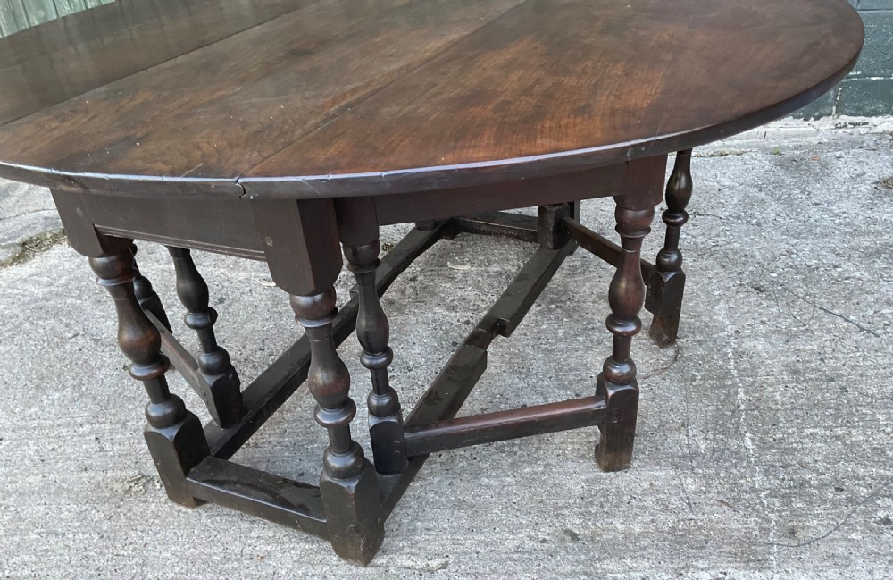 Underside view of a dark brown oak gateleg table showing baluster turned legs, stretchers, hand-forged iron hinges, and hinged drop leaves. View VIII
