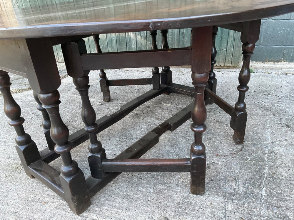 Underside view of a dark brown oak gateleg table showing baluster turned legs, stretchers, hand-forged iron hinges, and hinged drop leaves. View IX