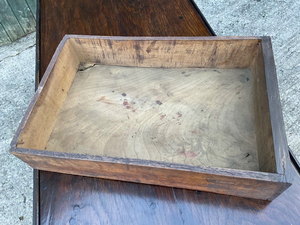 Underside view of a dark brown oak gateleg table showing baluster turned legs, stretchers, hand-forged iron hinges, and hinged drop leaves. View XI