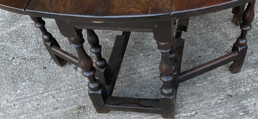Underside view of a dark brown oak gateleg table showing baluster turned legs, stretchers, hand-forged iron hinges, and hinged drop leaves. View XIII