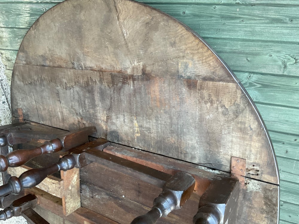 Underside view of a dark brown oak gateleg table showing baluster turned legs, stretchers, hand-forged iron hinges, and hinged drop leaves. View XVIII