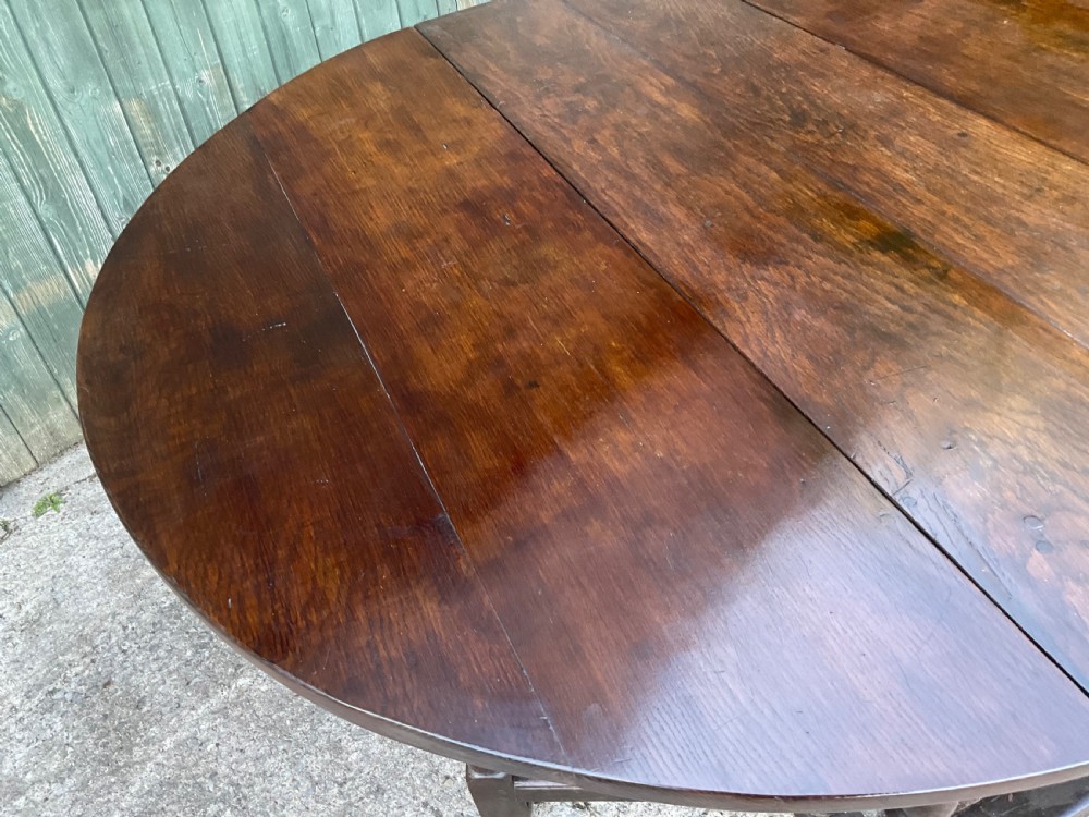 Underside view of a dark brown oak gateleg table showing baluster turned legs, stretchers, hand-forged iron hinges, and hinged drop leaves. View XIX