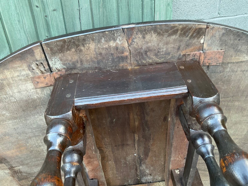 Underside view of a dark brown oak gateleg table showing baluster turned legs, stretchers, hand-forged iron hinges, and hinged drop leaves. View XX