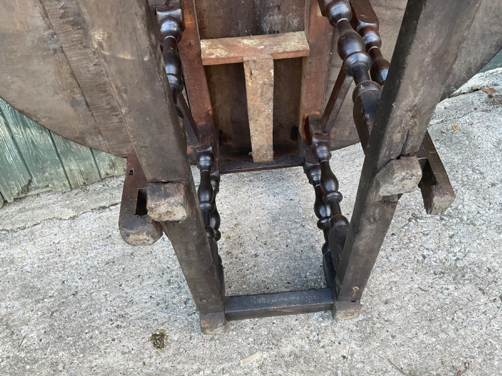 Underside view of a dark brown oak gateleg table showing baluster turned legs, stretchers, hand-forged iron hinges, and hinged drop leaves. View XXII