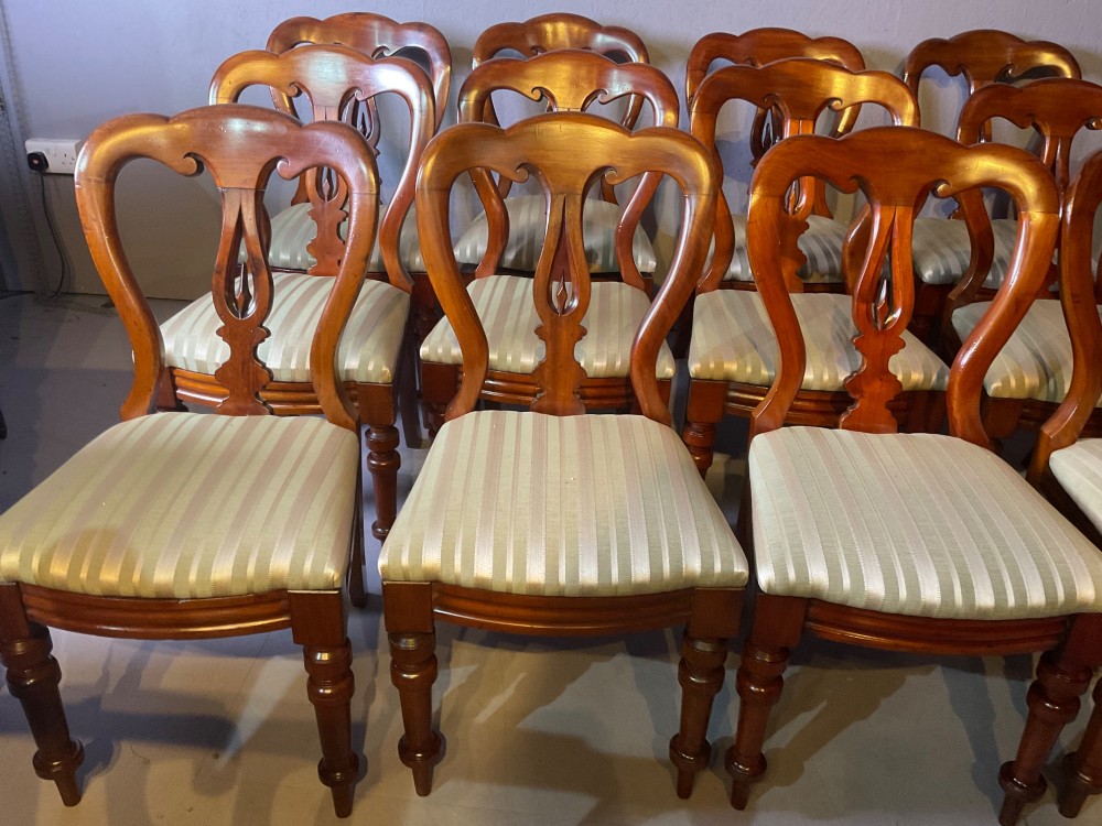 A set of twelve Victorian mahogany balloon back dining chairs featuring carved spear point splats and striped upholstered seats. View II