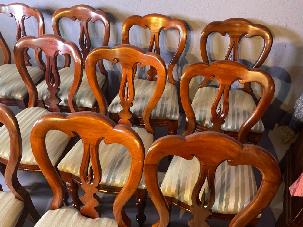 A set of twelve Victorian mahogany balloon back dining chairs featuring carved spear point splats and striped upholstered seats. View IV