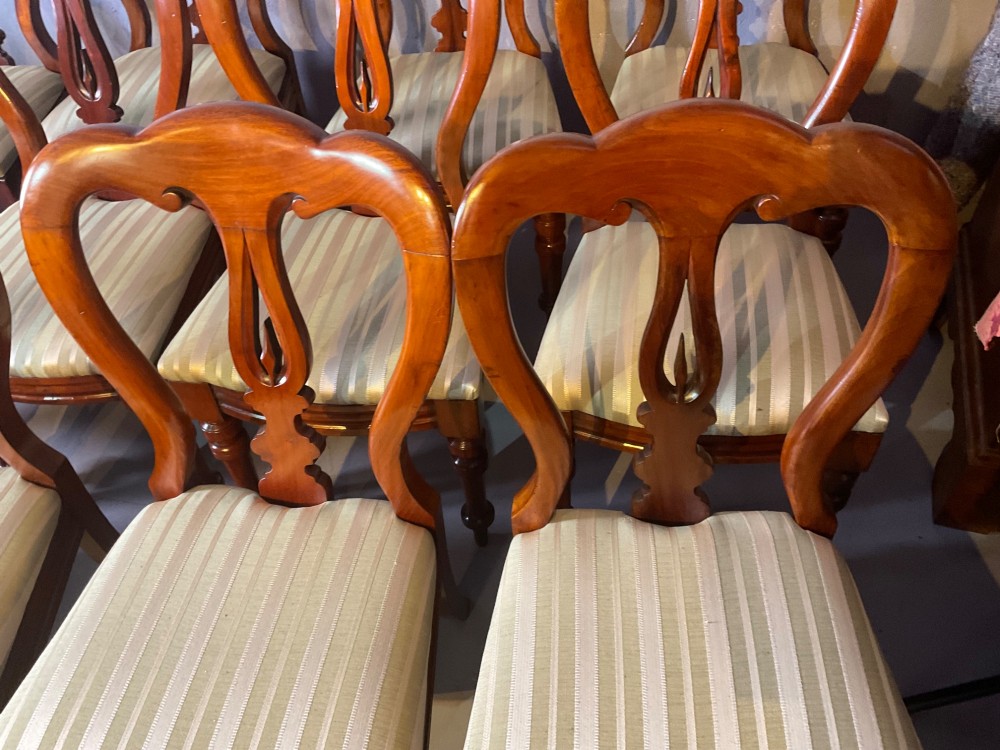 A set of twelve Victorian mahogany balloon back dining chairs featuring carved spear point splats and striped upholstered seats. View V