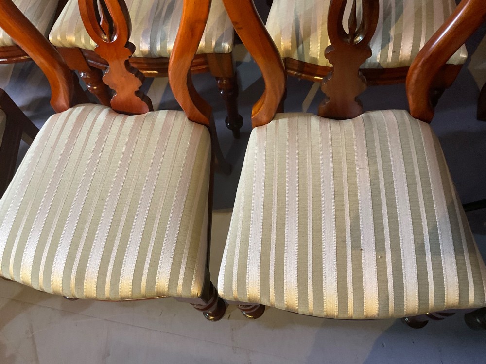 A set of twelve Victorian mahogany balloon back dining chairs featuring carved spear point splats and striped upholstered seats. View VI
