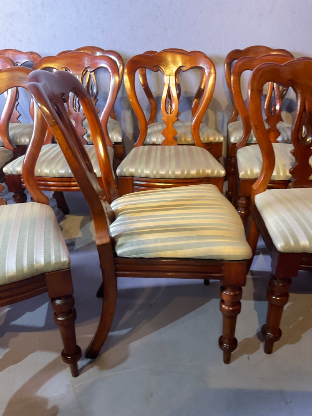 A set of twelve Victorian mahogany balloon back dining chairs featuring carved spear point splats and striped upholstered seats. View VIII