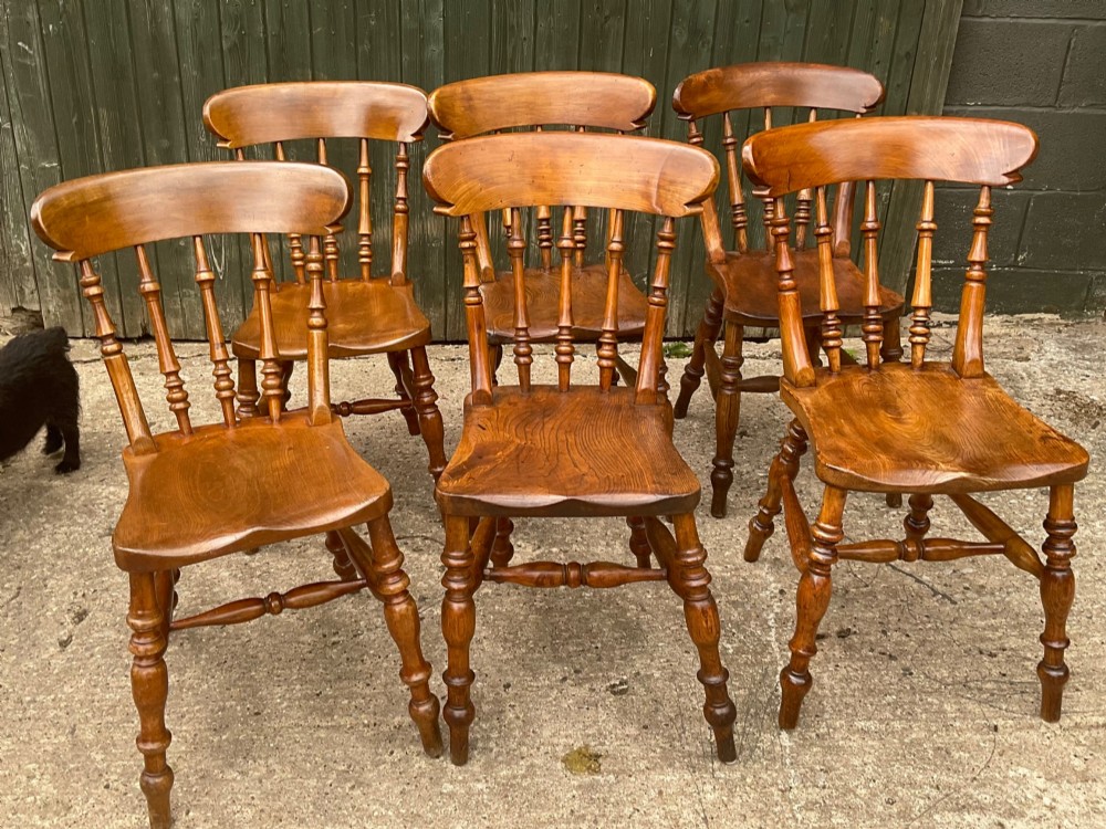A set of six warm brown wooden dining chairs featuring spindle backrests, contoured wooden seats, and turned legs.