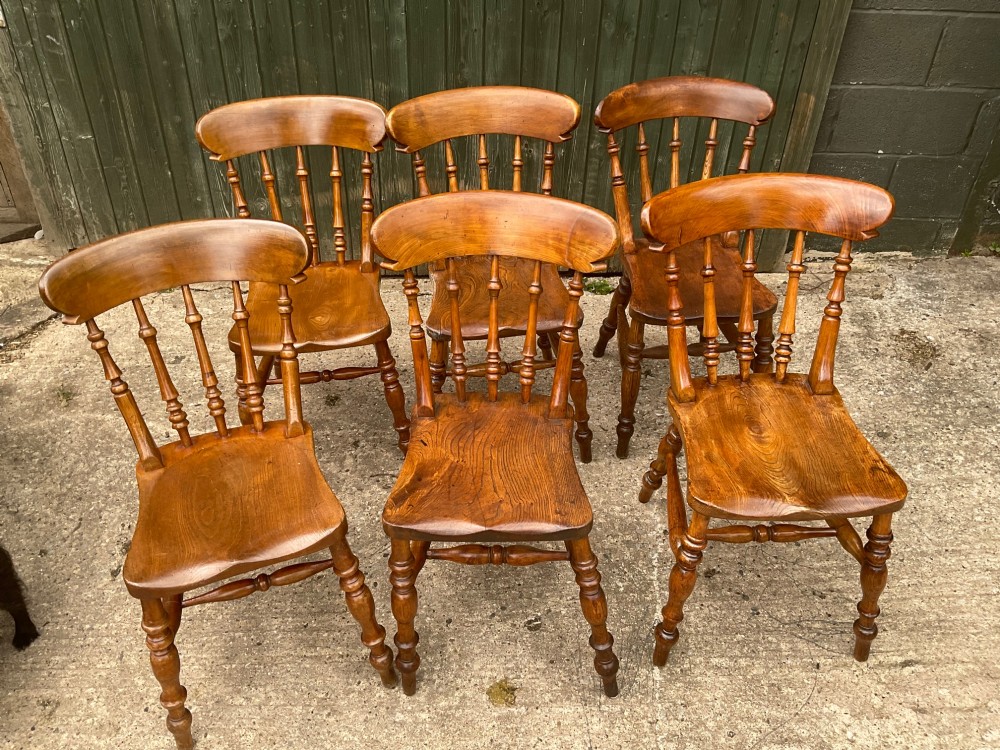 A set of six warm brown wooden dining chairs featuring spindle backrests, contoured wooden seats, and turned legs. View II