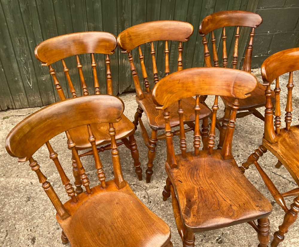 A set of six warm brown wooden dining chairs featuring spindle backrests, contoured wooden seats, and turned legs. View IV