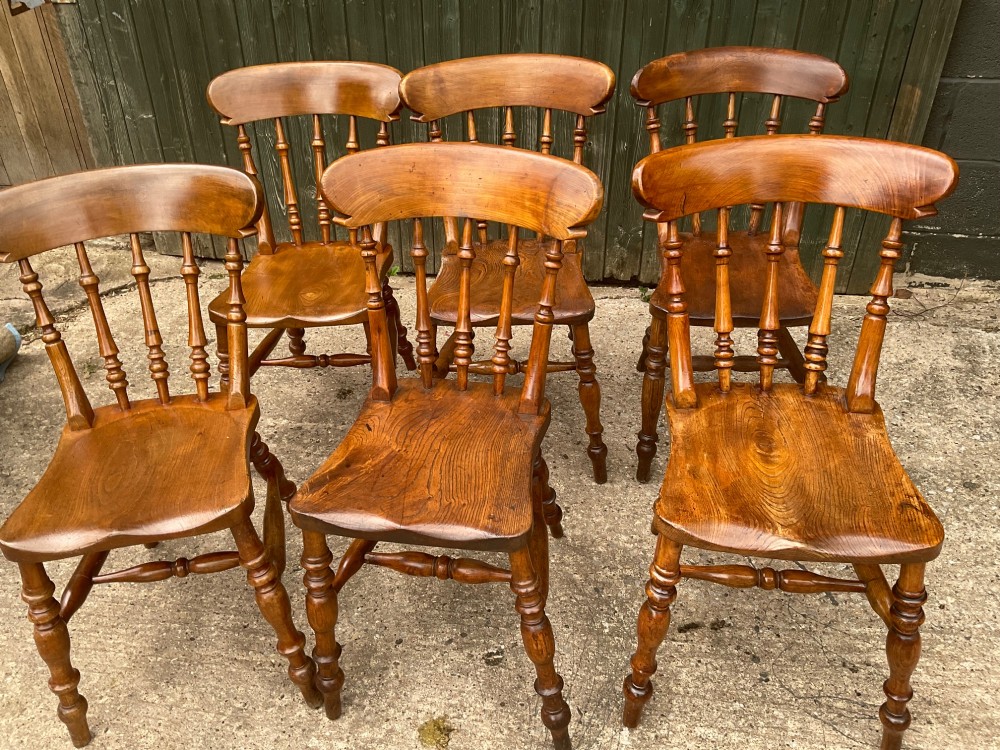 A set of six warm brown wooden dining chairs featuring spindle backrests, contoured wooden seats, and turned legs. View VI