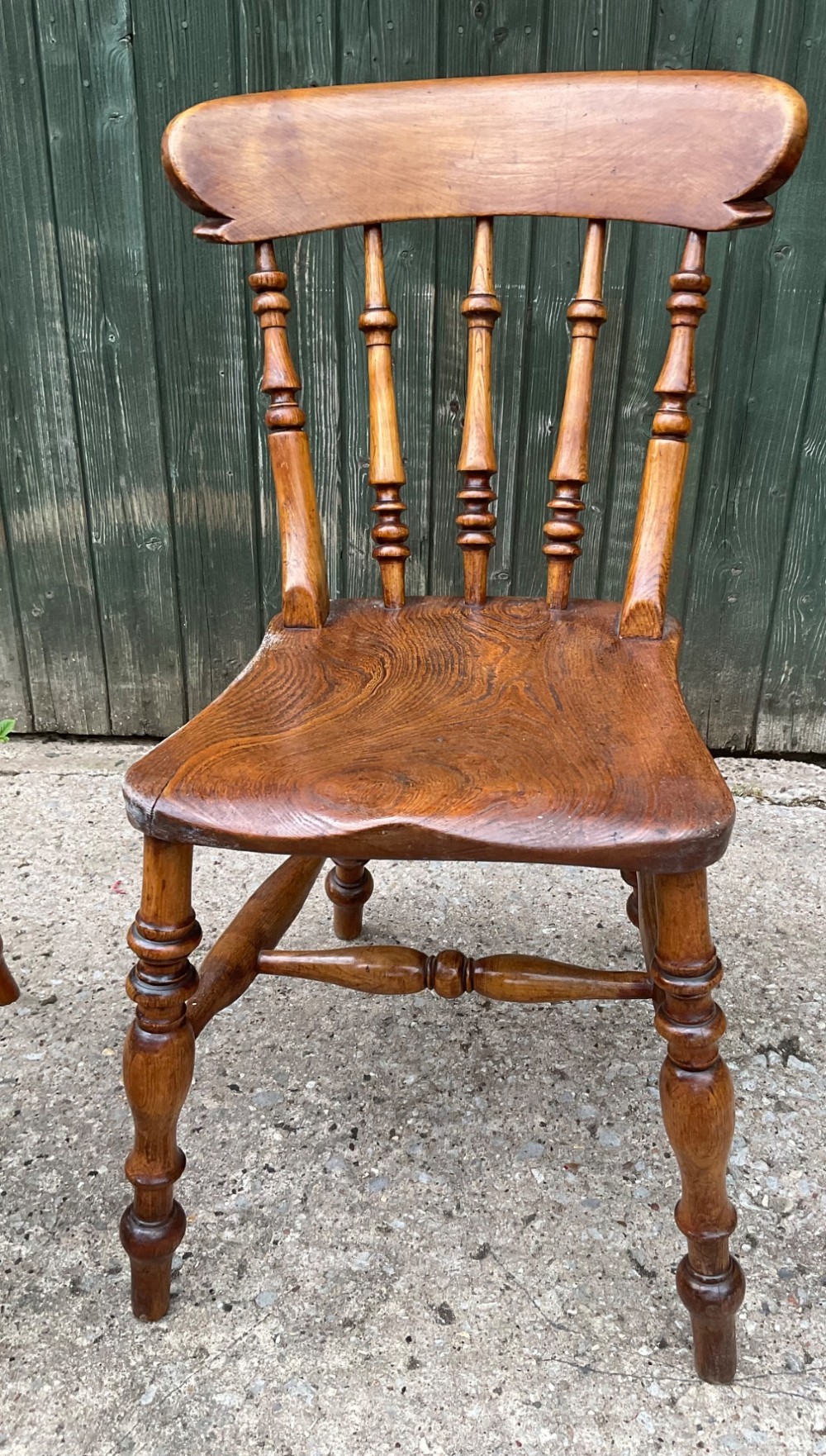 A set of six warm brown wooden dining chairs featuring spindle backrests, contoured wooden seats, and turned legs. View VII