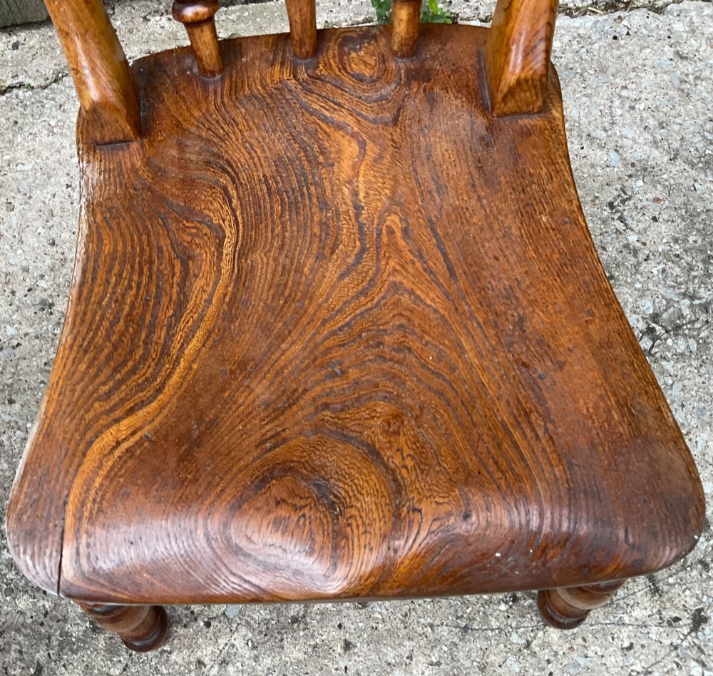 A set of six warm brown wooden dining chairs featuring spindle backrests, contoured wooden seats, and turned legs. View IX