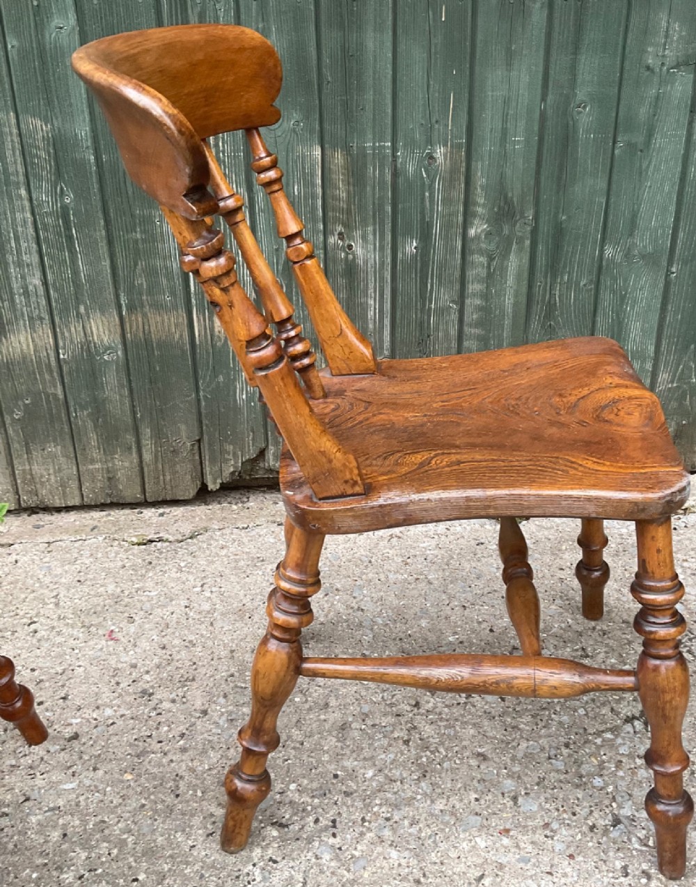 A set of six warm brown wooden dining chairs featuring spindle backrests, contoured wooden seats, and turned legs. View X