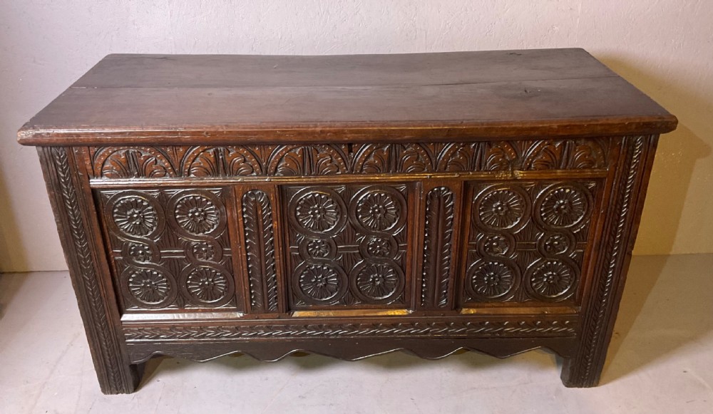 A seventeenth-century dark oak coffer featuring three relief-carved front panels with rosette motifs and a flat hinged lid.
