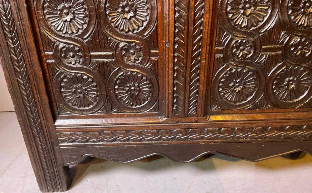 A seventeenth-century dark oak coffer featuring three relief-carved front panels with rosette motifs and a flat hinged lid. View II