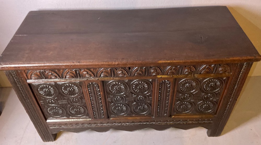 A seventeenth-century dark oak coffer featuring three relief-carved front panels with rosette motifs and a flat hinged lid. View IV
