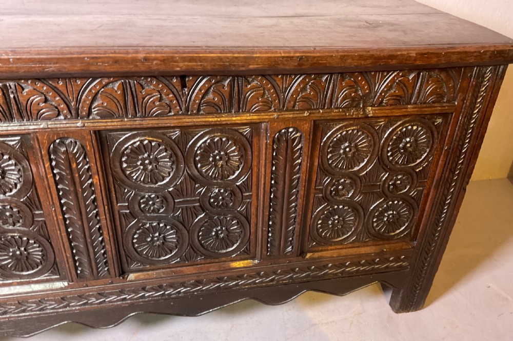 A seventeenth-century dark oak coffer featuring three relief-carved front panels with rosette motifs and a flat hinged lid. View V