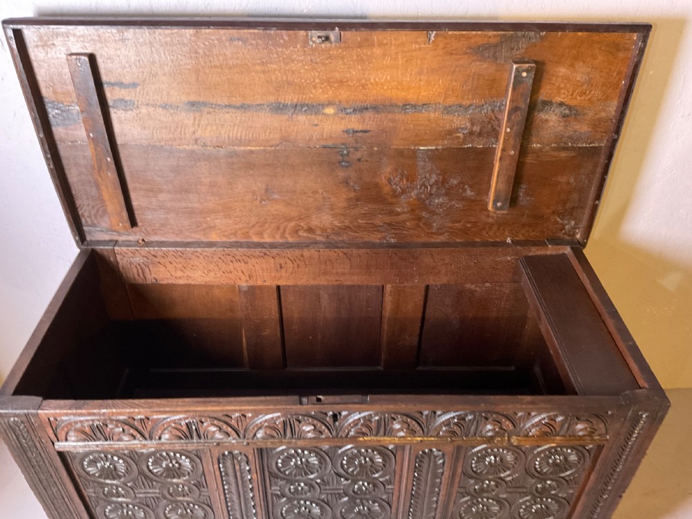 A seventeenth-century dark oak coffer featuring three relief-carved front panels with rosette motifs and a flat hinged lid. View VI
