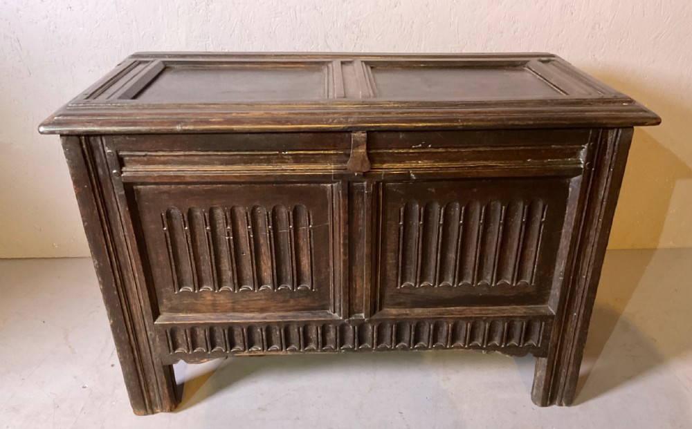 A dark oak 17th-century coffer featuring two carved linenfold front panels, a carved lower rail, and a framed hinged lid.
