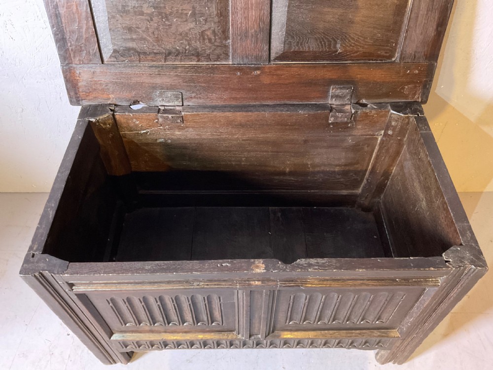 A dark oak 17th-century coffer featuring two carved linenfold front panels, a carved lower rail, and a framed hinged lid. View V
