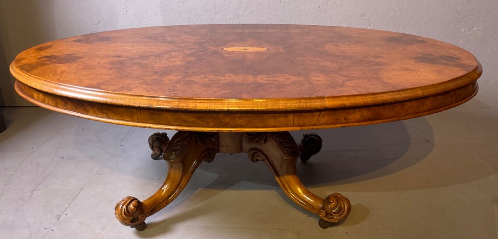 An oval burr walnut coffee table featuring central marquetry inlay, a moulded rim, and carved cabriole legs on brass castors.