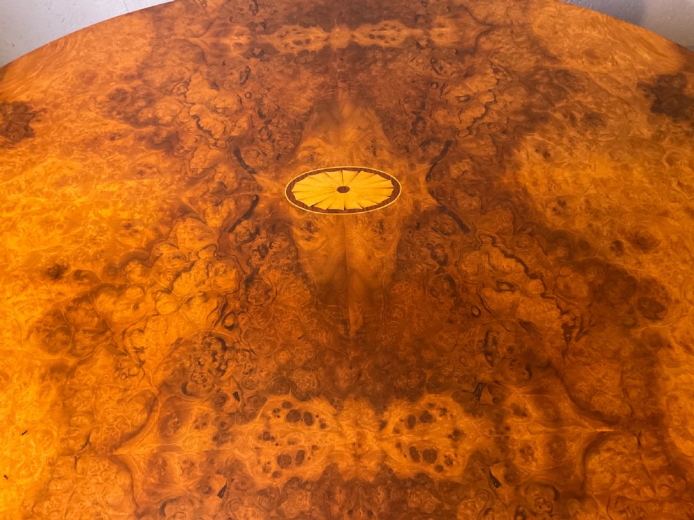 An oval burr walnut coffee table featuring central marquetry inlay, a moulded rim, and carved cabriole legs on brass castors. View III