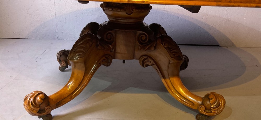 An oval burr walnut coffee table featuring central marquetry inlay, a moulded rim, and carved cabriole legs on brass castors. View IV