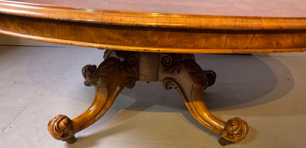 An oval burr walnut coffee table featuring central marquetry inlay, a moulded rim, and carved cabriole legs on brass castors. View V