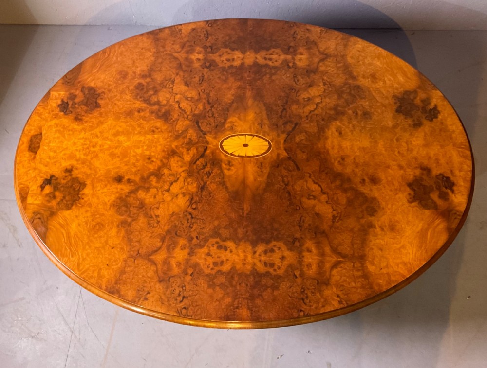 An oval burr walnut coffee table featuring central marquetry inlay, a moulded rim, and carved cabriole legs on brass castors. View VIII