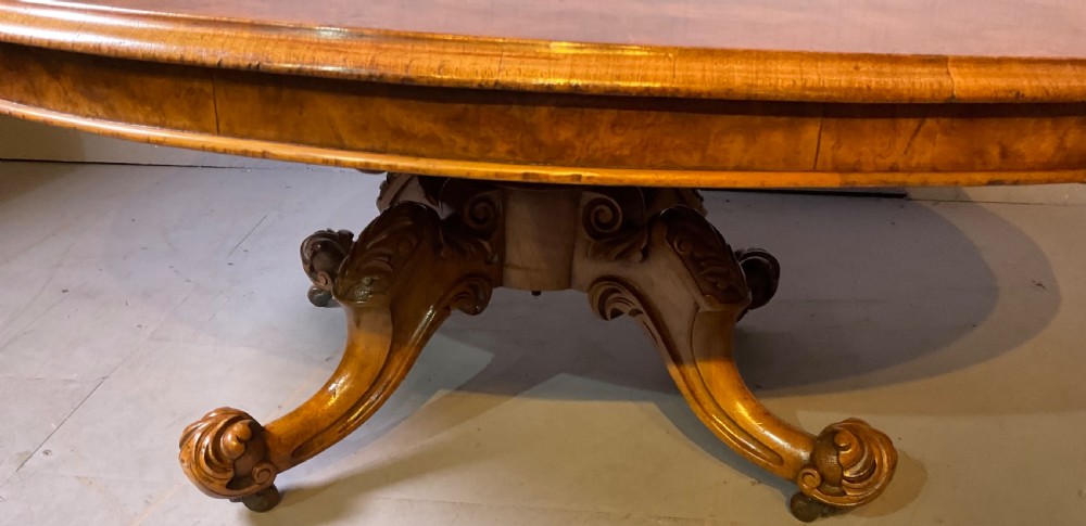 An oval burr walnut coffee table featuring central marquetry inlay, a moulded rim, and carved cabriole legs on brass castors. View IX