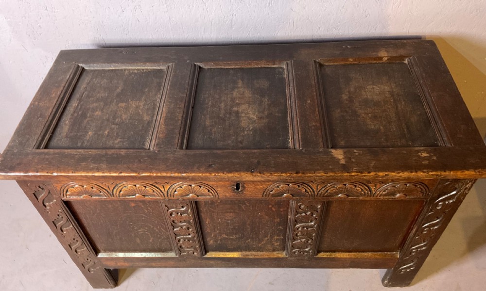 A dark carved 17th-century oak coffer featuring three panelled sections, a hinged lid, and decorative lunette carving along the frieze. View III