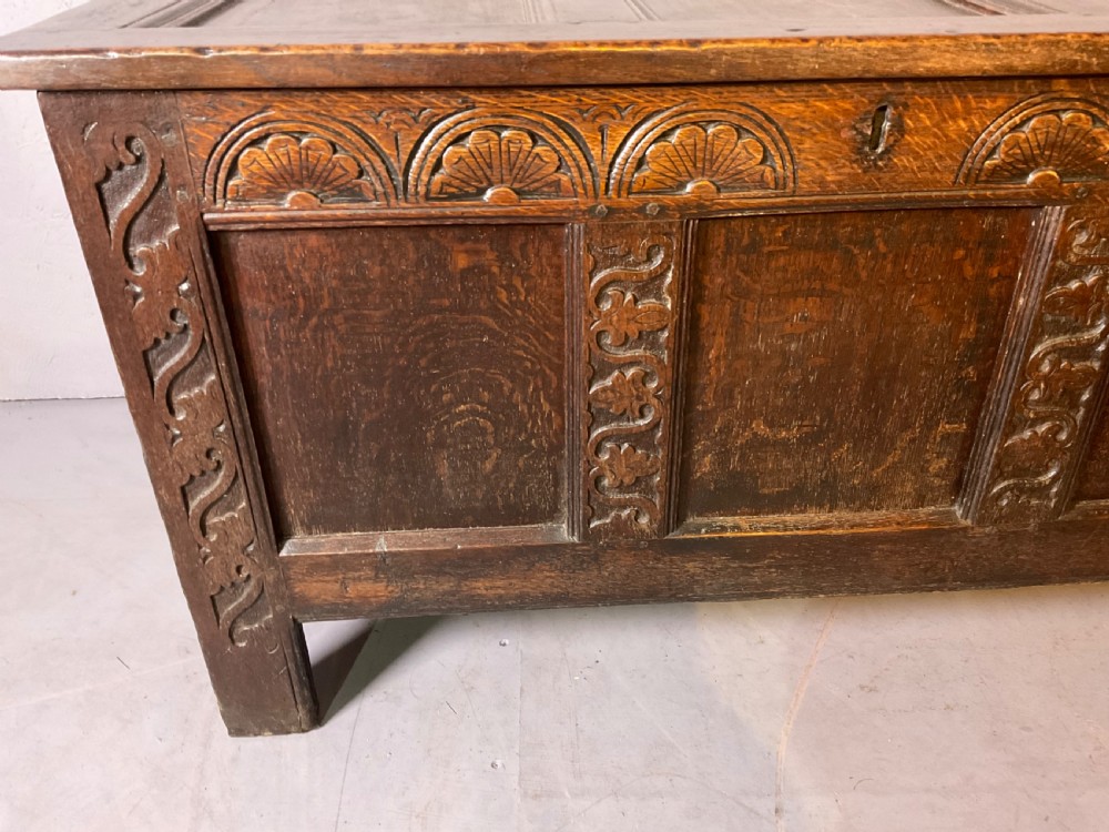 A dark carved 17th-century oak coffer featuring three panelled sections, a hinged lid, and decorative lunette carving along the frieze. View IV