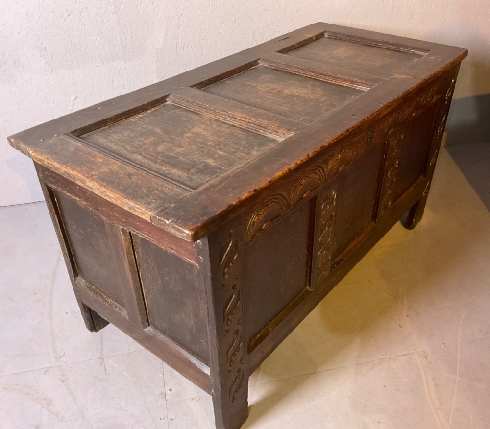 A dark carved 17th-century oak coffer featuring three panelled sections, a hinged lid, and decorative lunette carving along the frieze. View VI