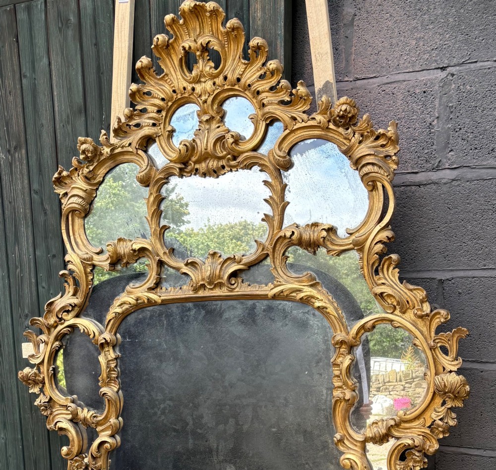 An ornate Georgian Rococo carved giltwood overmantel mirror featuring scrollwork, leaf motifs, and multi-pane glass panels. View III