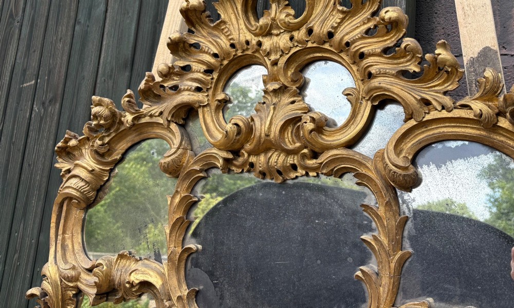 An ornate Georgian Rococo carved giltwood overmantel mirror featuring scrollwork, leaf motifs, and multi-pane glass panels. View V