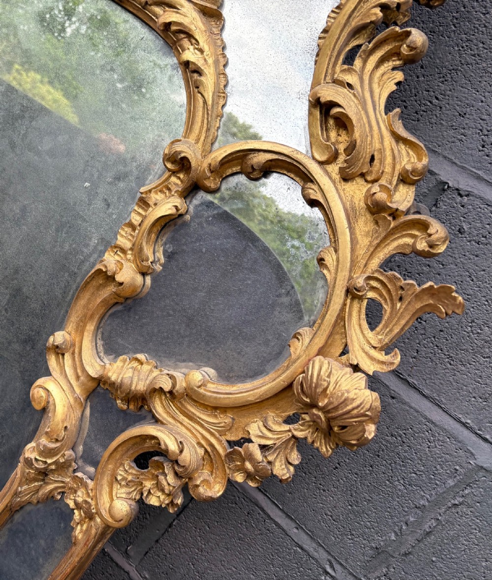 An ornate Georgian Rococo carved giltwood overmantel mirror featuring scrollwork, leaf motifs, and multi-pane glass panels. View VII