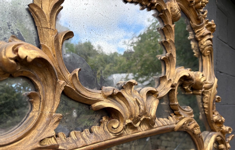 An ornate Georgian Rococo carved giltwood overmantel mirror featuring scrollwork, leaf motifs, and multi-pane glass panels. View VIII