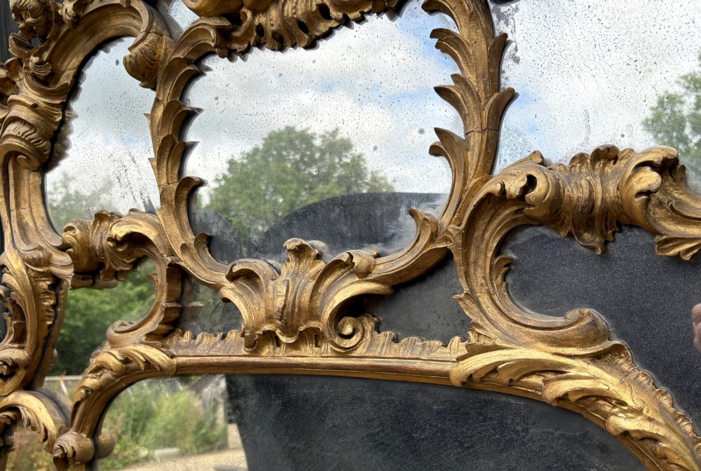 An ornate Georgian Rococo carved giltwood overmantel mirror featuring scrollwork, leaf motifs, and multi-pane glass panels. View XIV