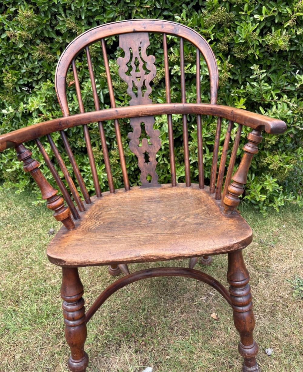 An antique yew wood low-back Windsor armchair featuring a pierced back splat, turned spindles, a contoured seat, and turned legs with a crinoline stretcher.