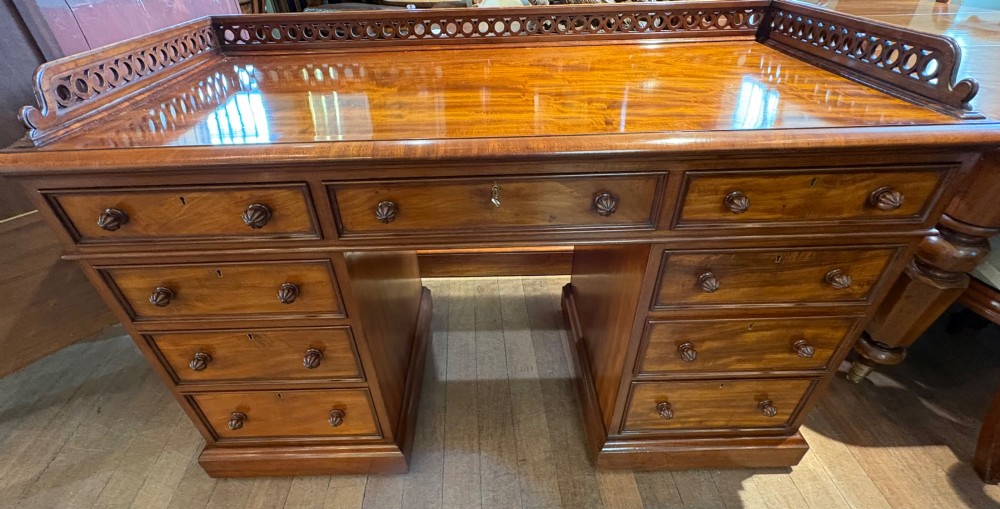 A nineteenth-century mahogany pedestal desk featuring nine drawers with turned wooden handles and a carved pierced gallery top.