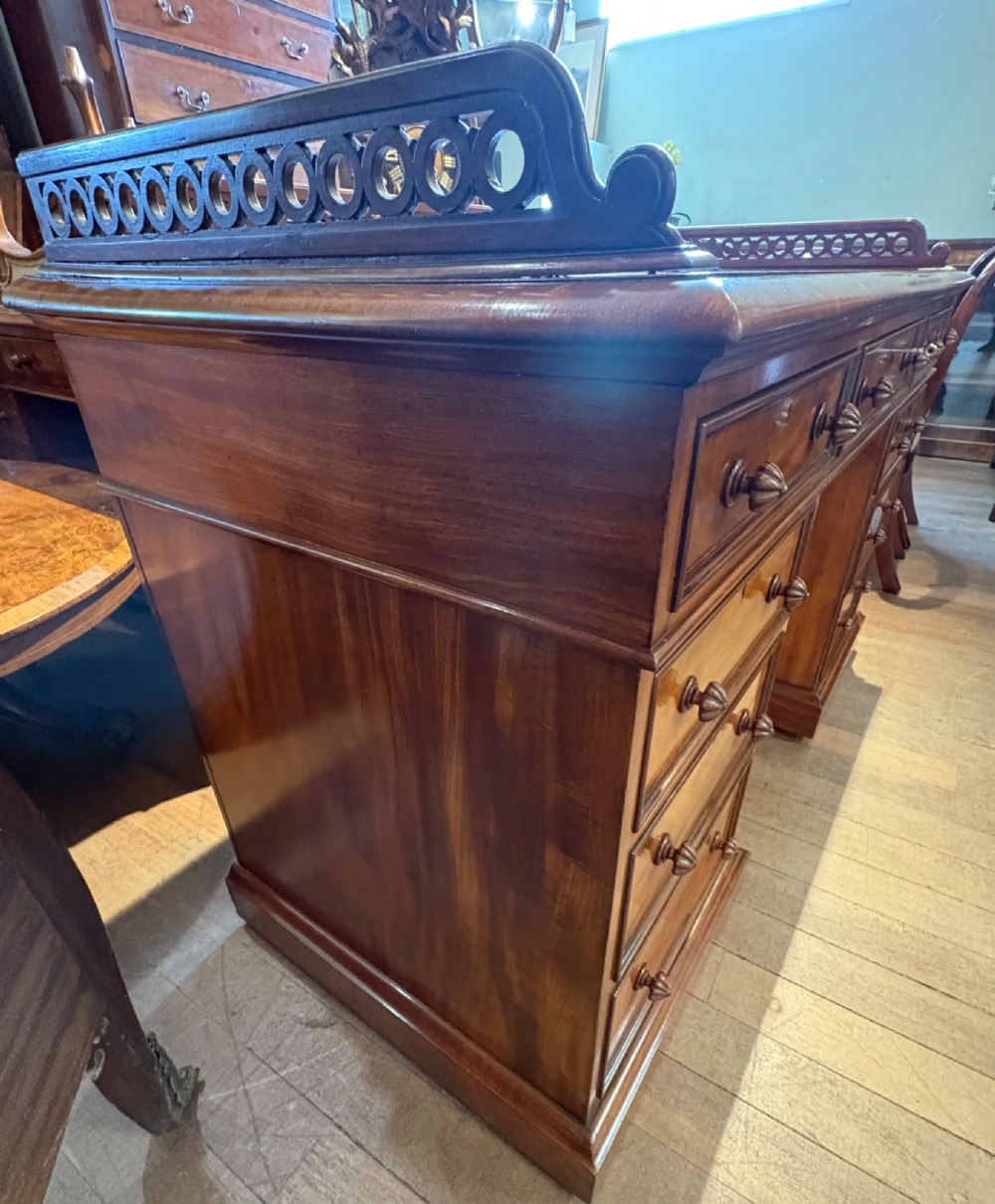A nineteenth-century mahogany pedestal desk featuring nine drawers with turned wooden handles and a carved pierced gallery top. View IV