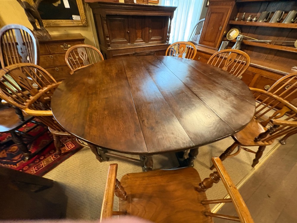 Underside view of a dark brown oak gateleg table showing baluster turned legs, stretchers, hand-forged iron hinges, and hinged drop leaves. View XIV
