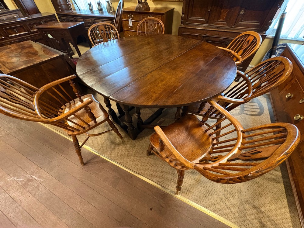 Underside view of a dark brown oak gateleg table showing baluster turned legs, stretchers, hand-forged iron hinges, and hinged drop leaves. View XV