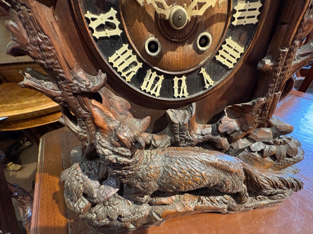 An intricately hand-carved dark wood Black Forest cuckoo clock featuring a bird atop a nest, a framed dial with Roman numerals, and a fox figure at the base. View II