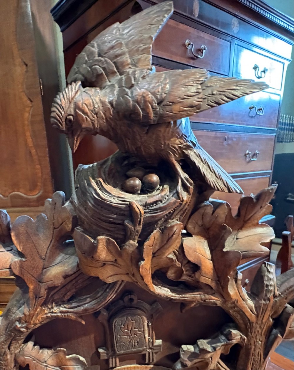 An intricately hand-carved dark wood Black Forest cuckoo clock featuring a bird atop a nest, a framed dial with Roman numerals, and a fox figure at the base. View IV